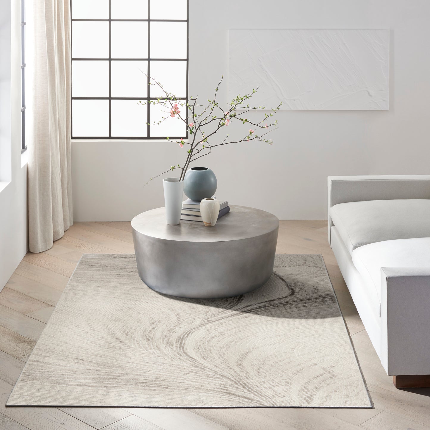Light minimalist living room with a modern rug, grid window, and decorative vases with blossoming branches.