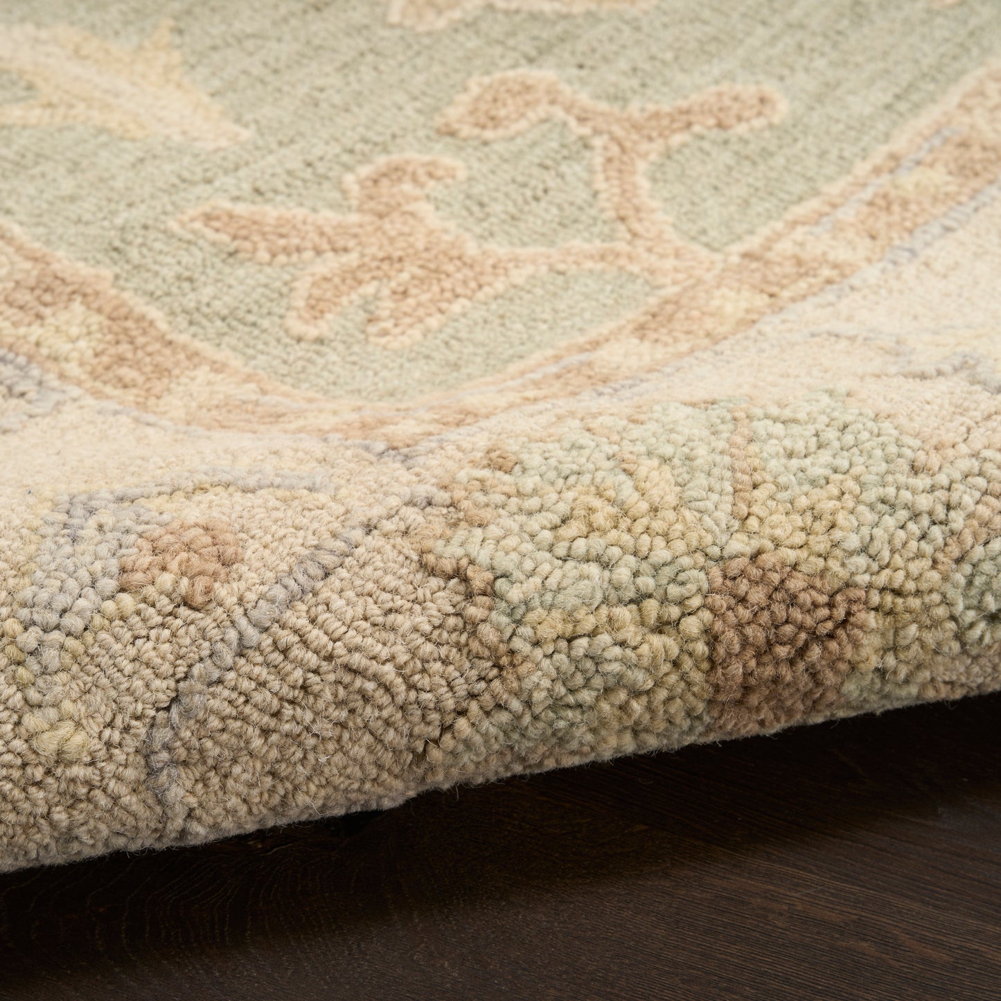 Close-up of a textured boucle-pile rug edge in beige with pastel green and peach motifs on a dark floor.
