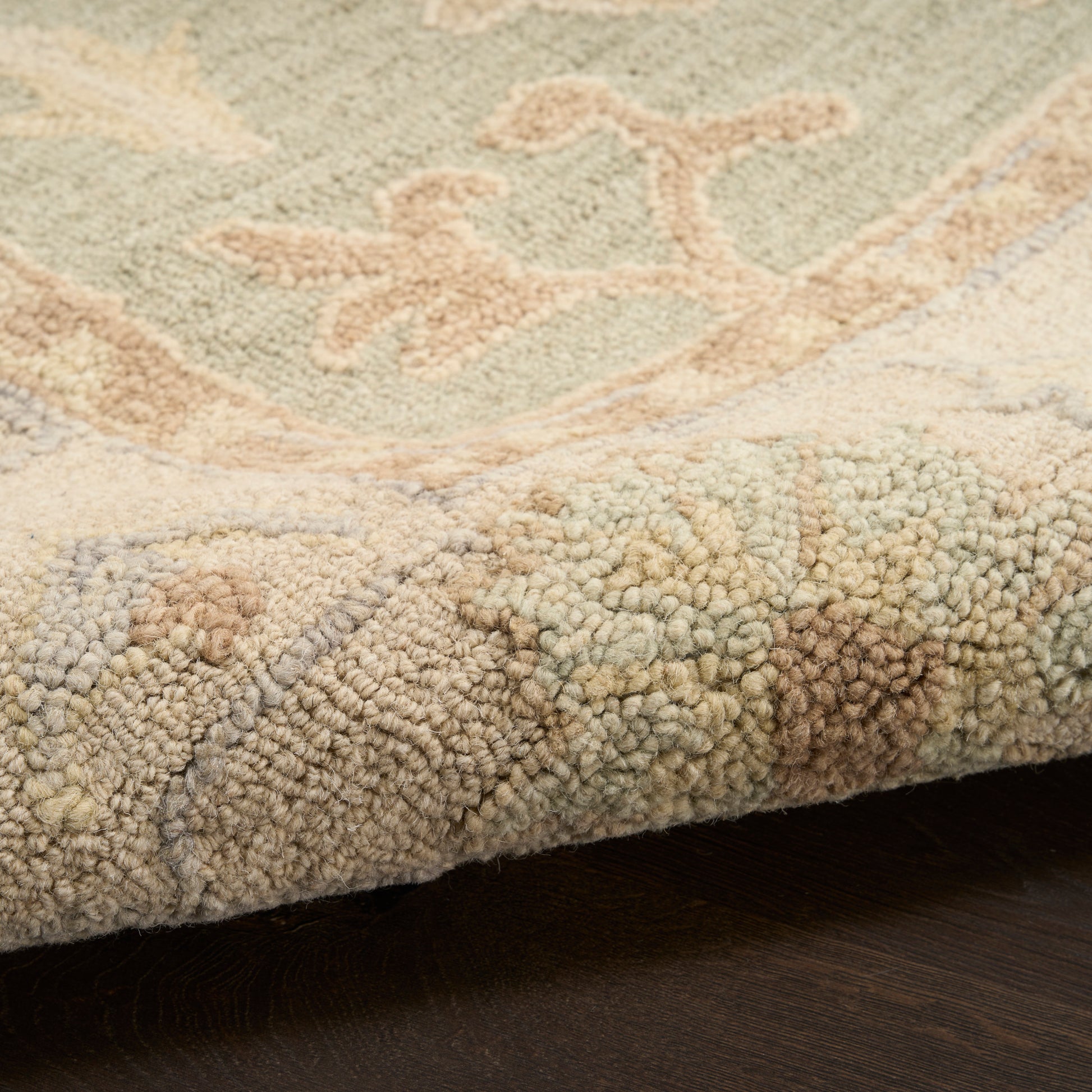 Close-up of a textured boucle-pile rug edge in beige with pastel green and peach motifs on a dark floor.