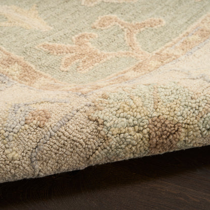 Close-up of a textured boucle-pile rug edge in beige with pastel green and peach motifs on a dark floor.