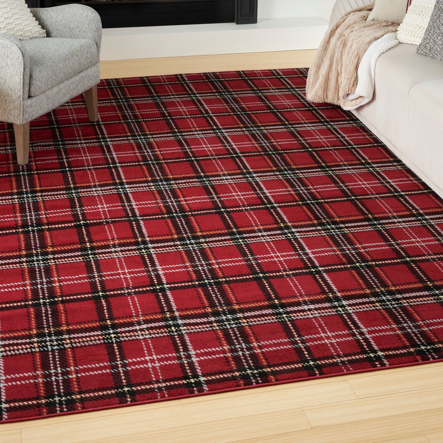 Red plaid area rug with black and white lines on light wood floor, gray armchair left and beige sofa with throw blankets.