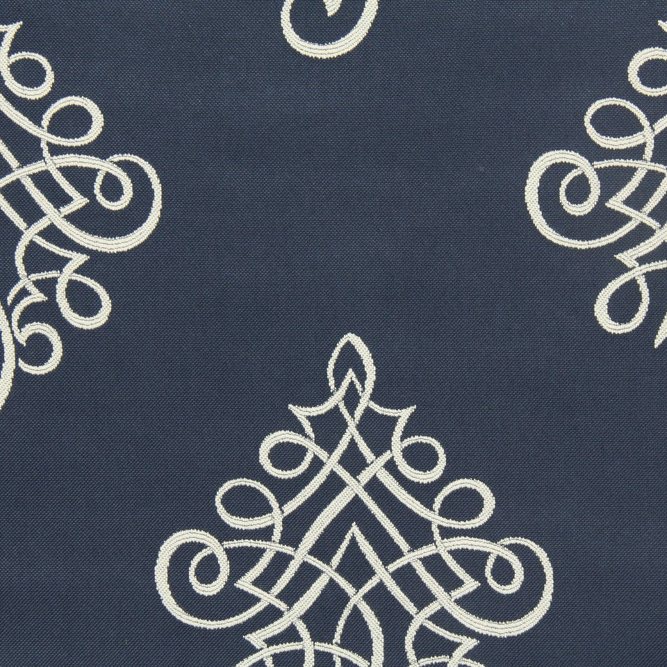 Navy upholstery fabric with white embroidered scrollwork motifs in a symmetrical ornate pattern; elegant decorative textile.
