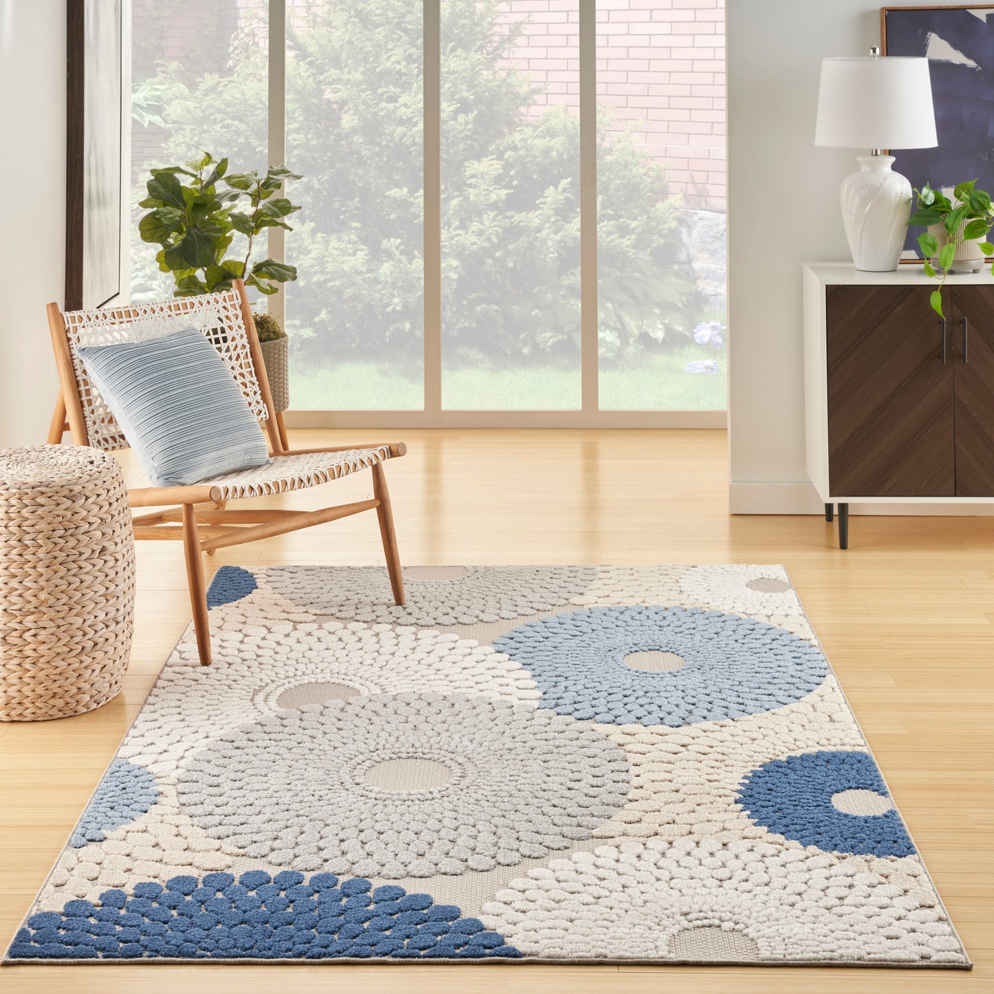Living room rug with large circular crochet patterns in blue, gray and beige; wood chair with blue cushion and woven pouf.