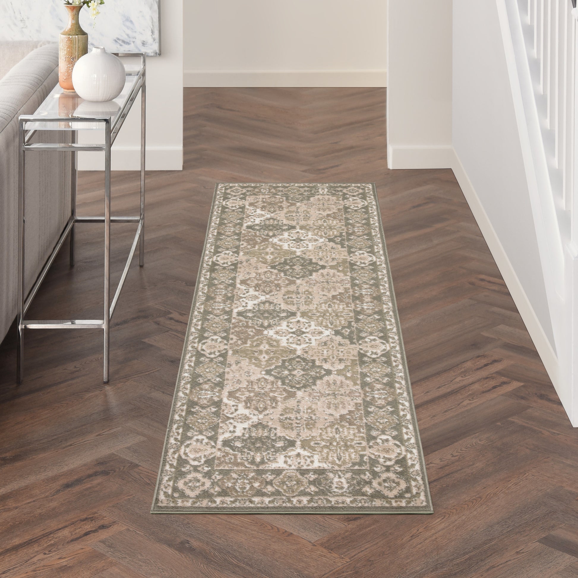Beige-and-gray oriental rug runner on a dark herringbone hallway floor beside a metal console table with a vase.