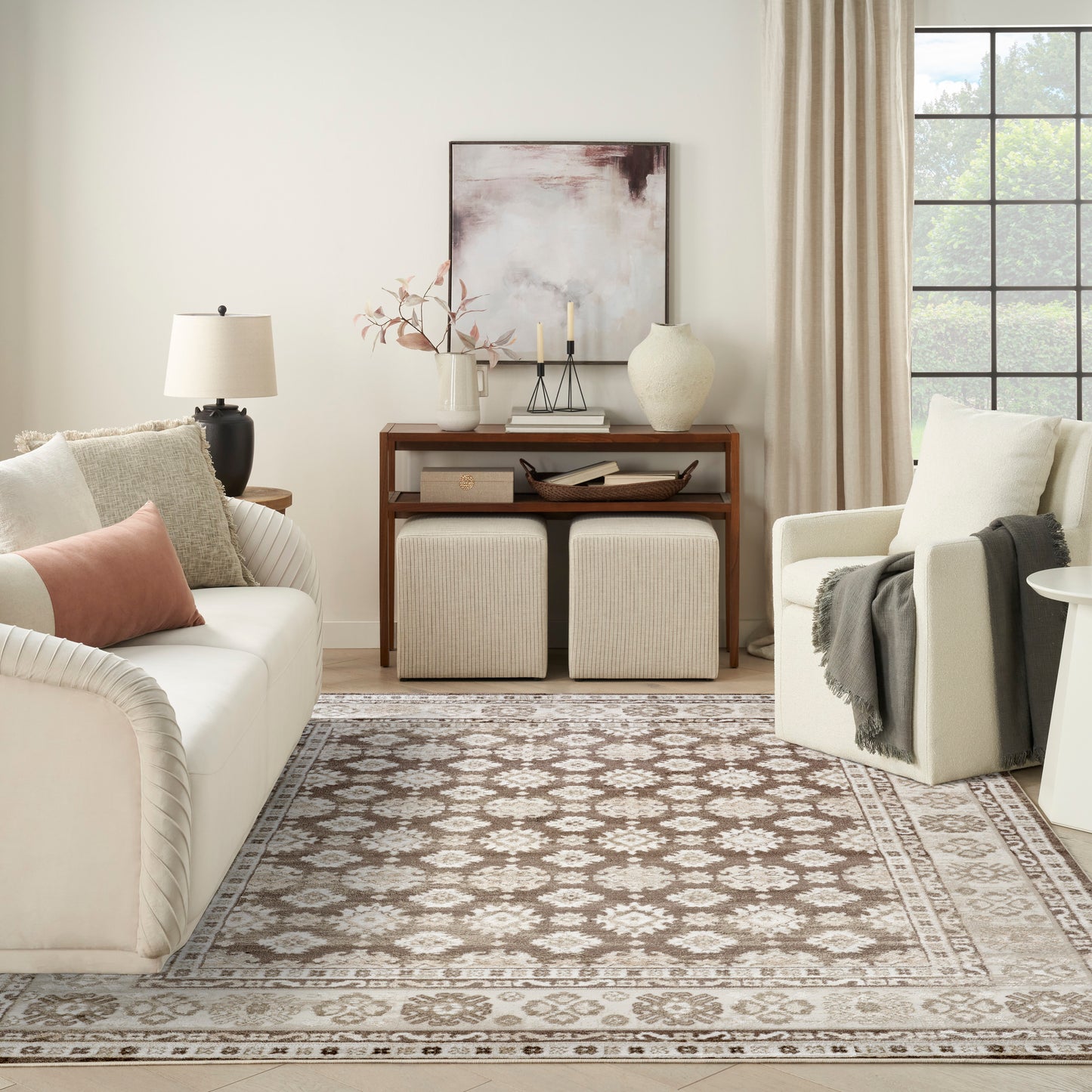Neutral living room with cream sofa, beige armchair, wooden console, two woven ottomans, and a patterned beige rug.