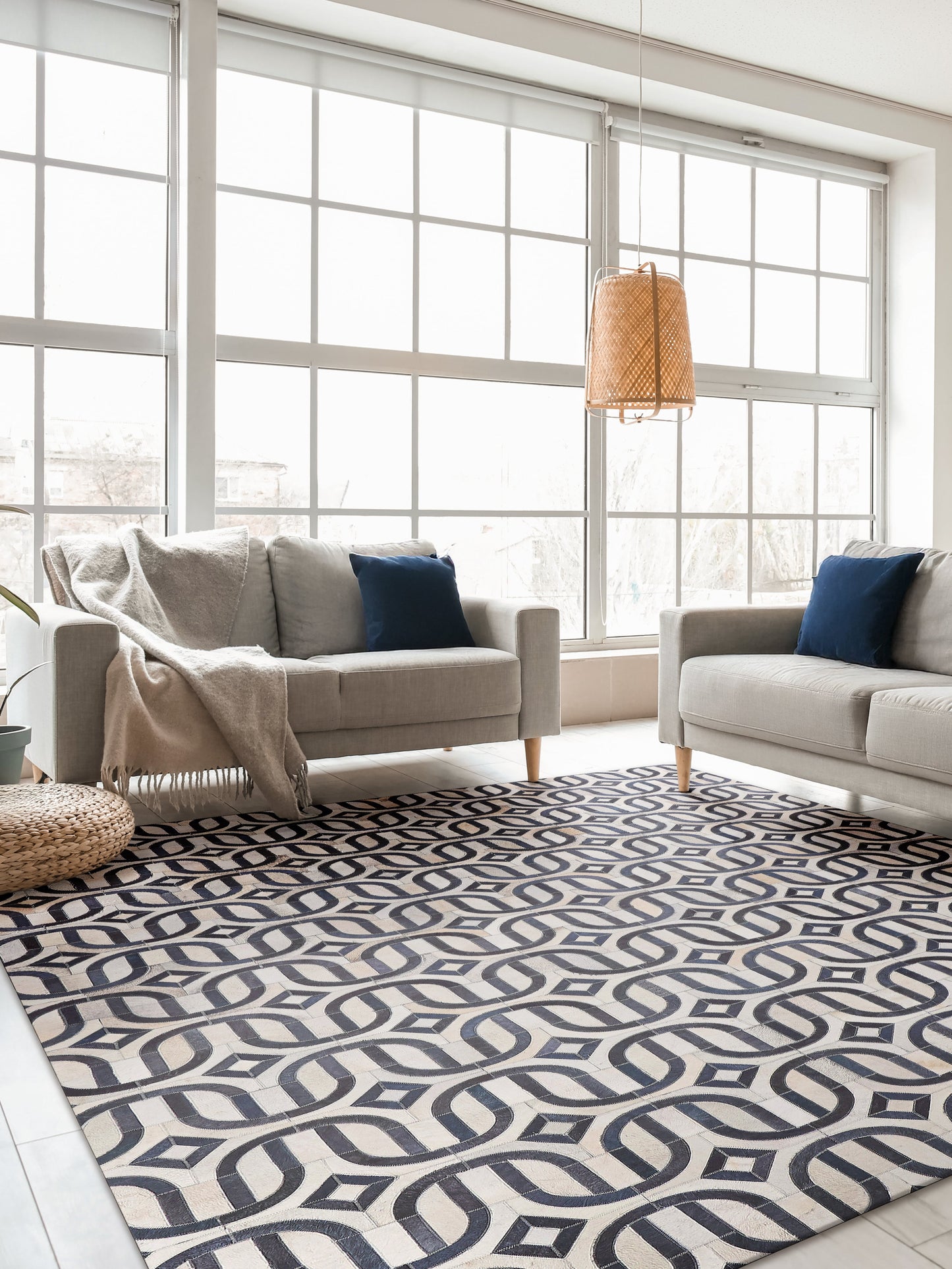 Bright living room with large grid windows, two beige sofas, navy cushions, woven pendant light, and a navy-cream geometric rug.