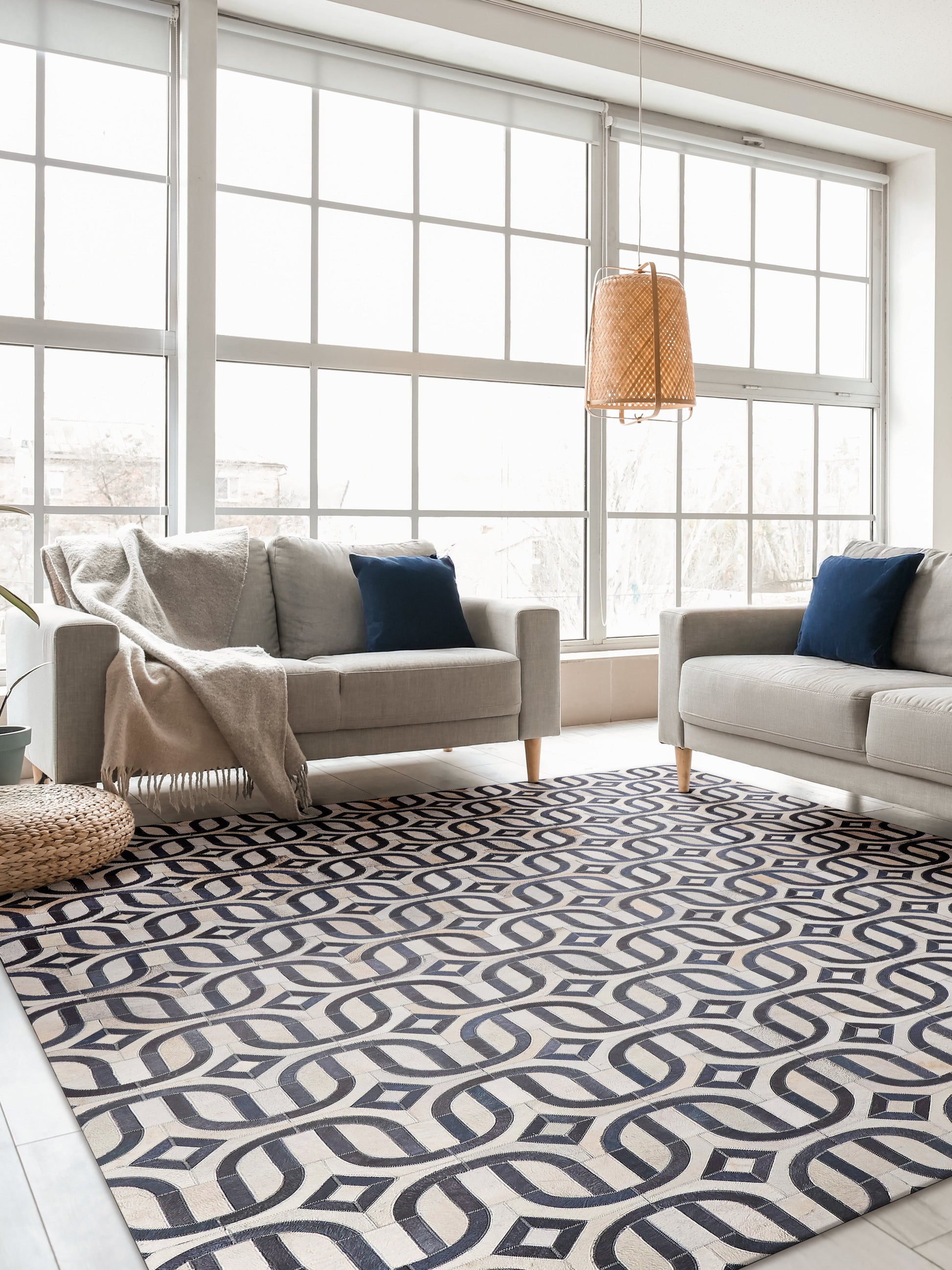 Bright living room with large grid windows, two beige sofas, navy cushions, woven pendant light, and a navy-cream geometric rug.