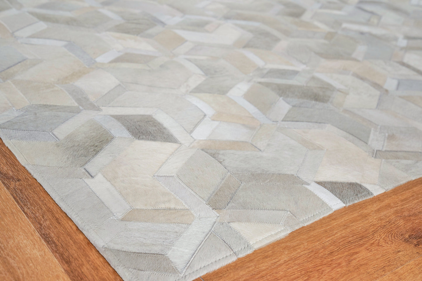 Geometric area rug in grey, taupe and beige patchwork hexagons on a warm wood floor