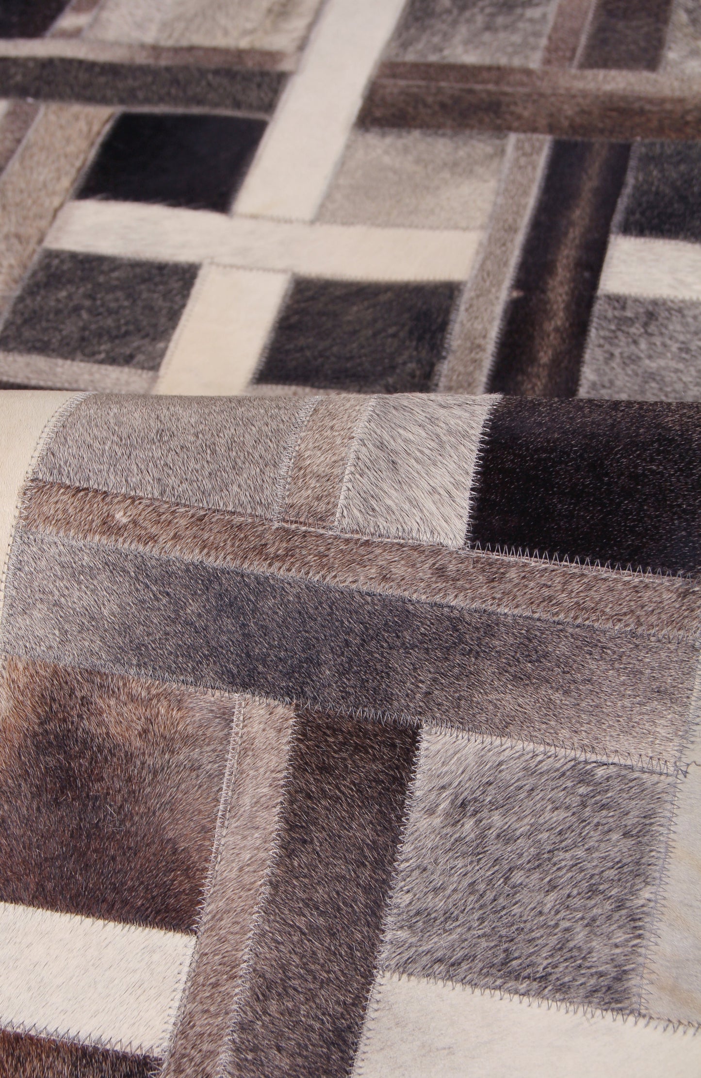 Patchwork natural-hide indoor area rug in neutral browns, creams and blacks with square blocks and hand-stitched detailing.