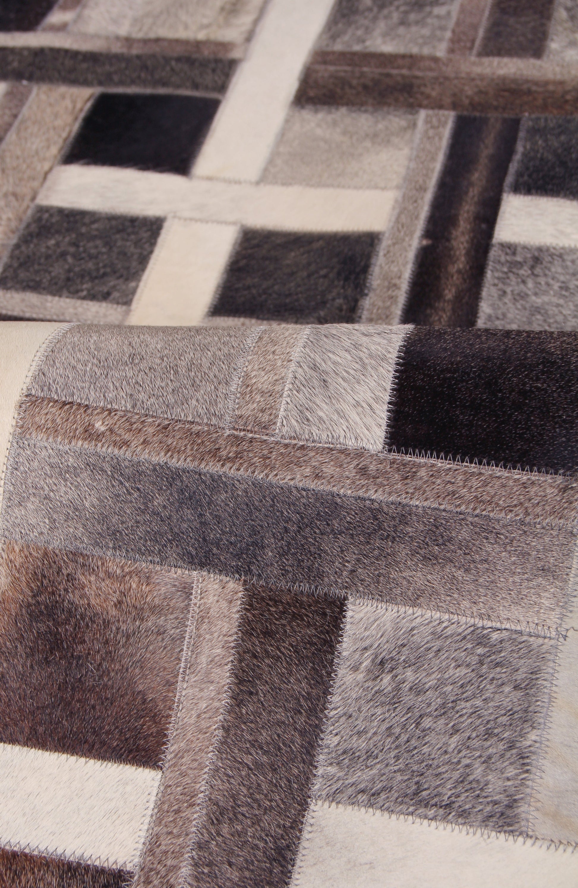 Patchwork natural-hide indoor area rug in neutral browns, creams and blacks with square blocks and hand-stitched detailing.