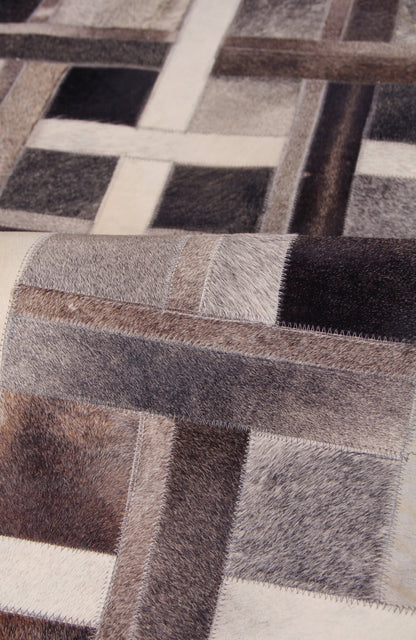 Patchwork natural-hide indoor area rug in neutral browns, creams and blacks with square blocks and hand-stitched detailing.