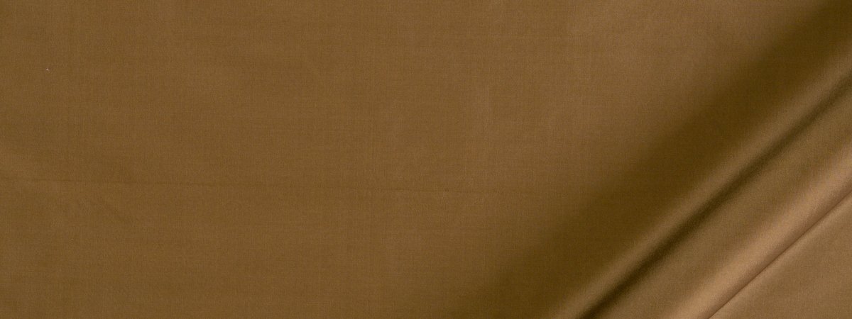 Close-up of tan brown fabric with a diagonal seam, suggesting a leather bag or wallet.