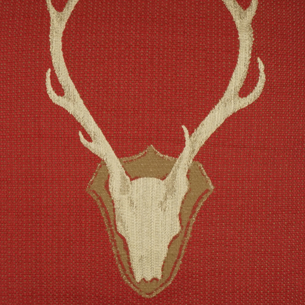 Red fabric pillow featuring a beige deer skull and antlers atop a brown shield motif.