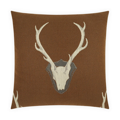Brown textured square pillow with white deer skull and antlers over a shield motif.