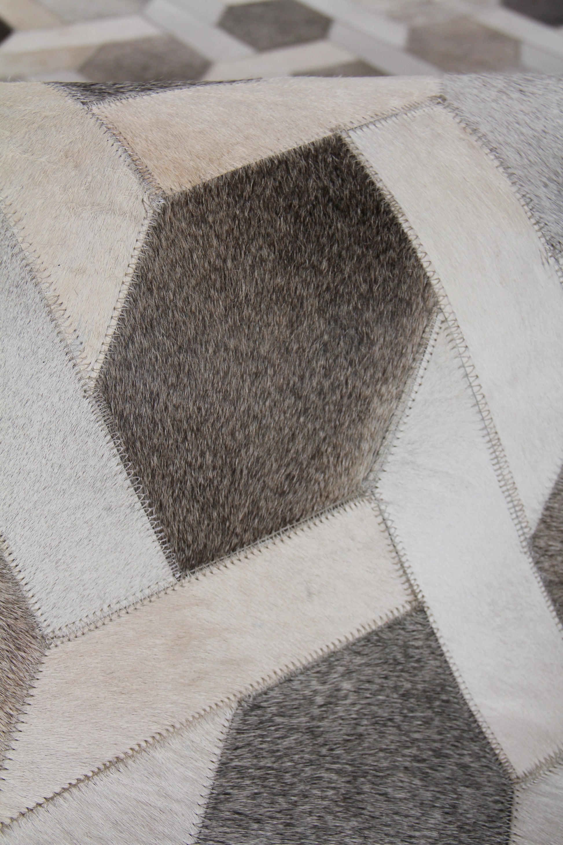 Geometric patchwork natural hide rug with hexagon patches in cream, beige, taupe and gray; hand-stitched seams.