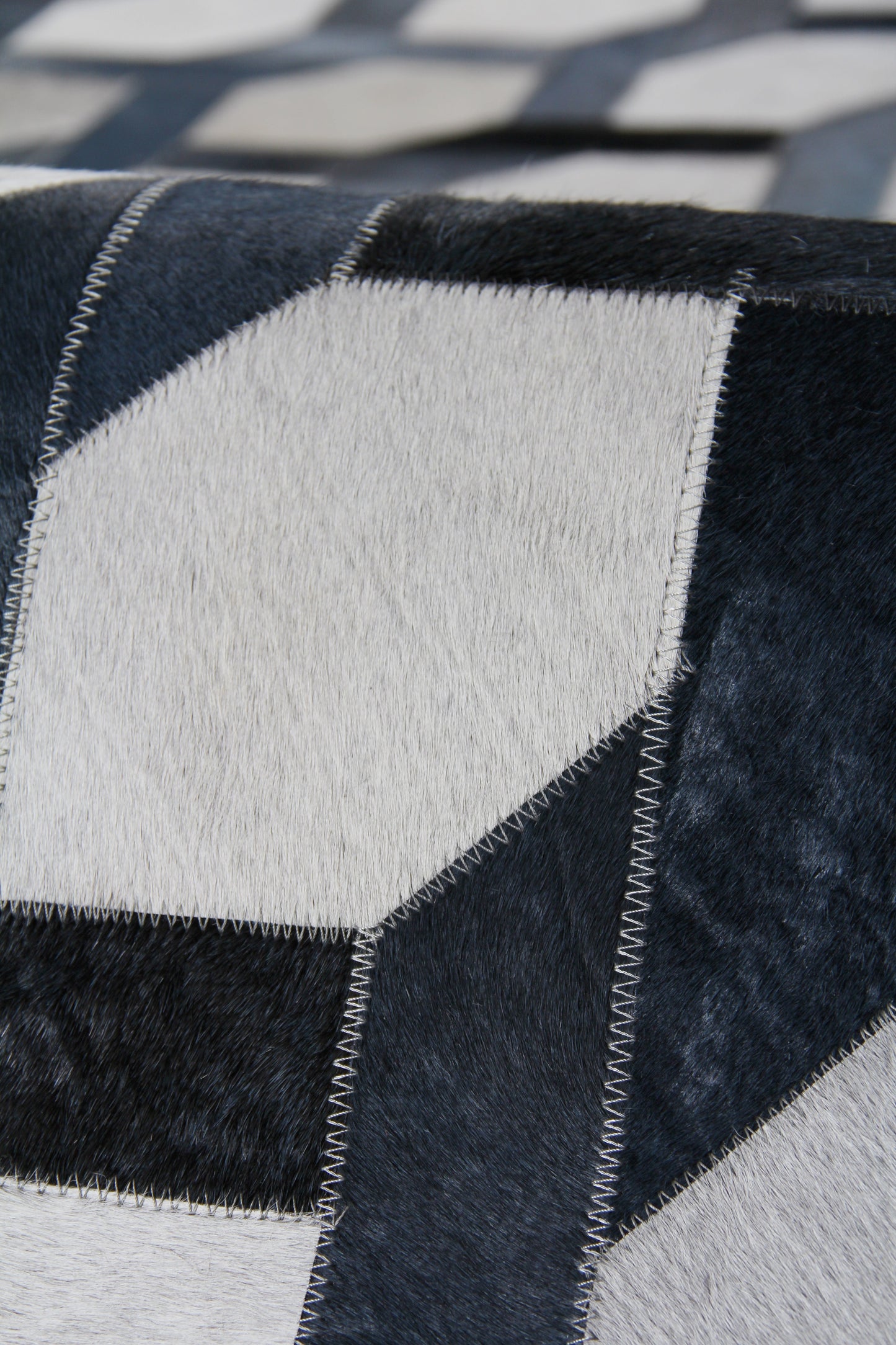 Patchwork natural hide rug in navy blue and white panels with white zigzag stitching and plush fur texture, 5' x 8'.