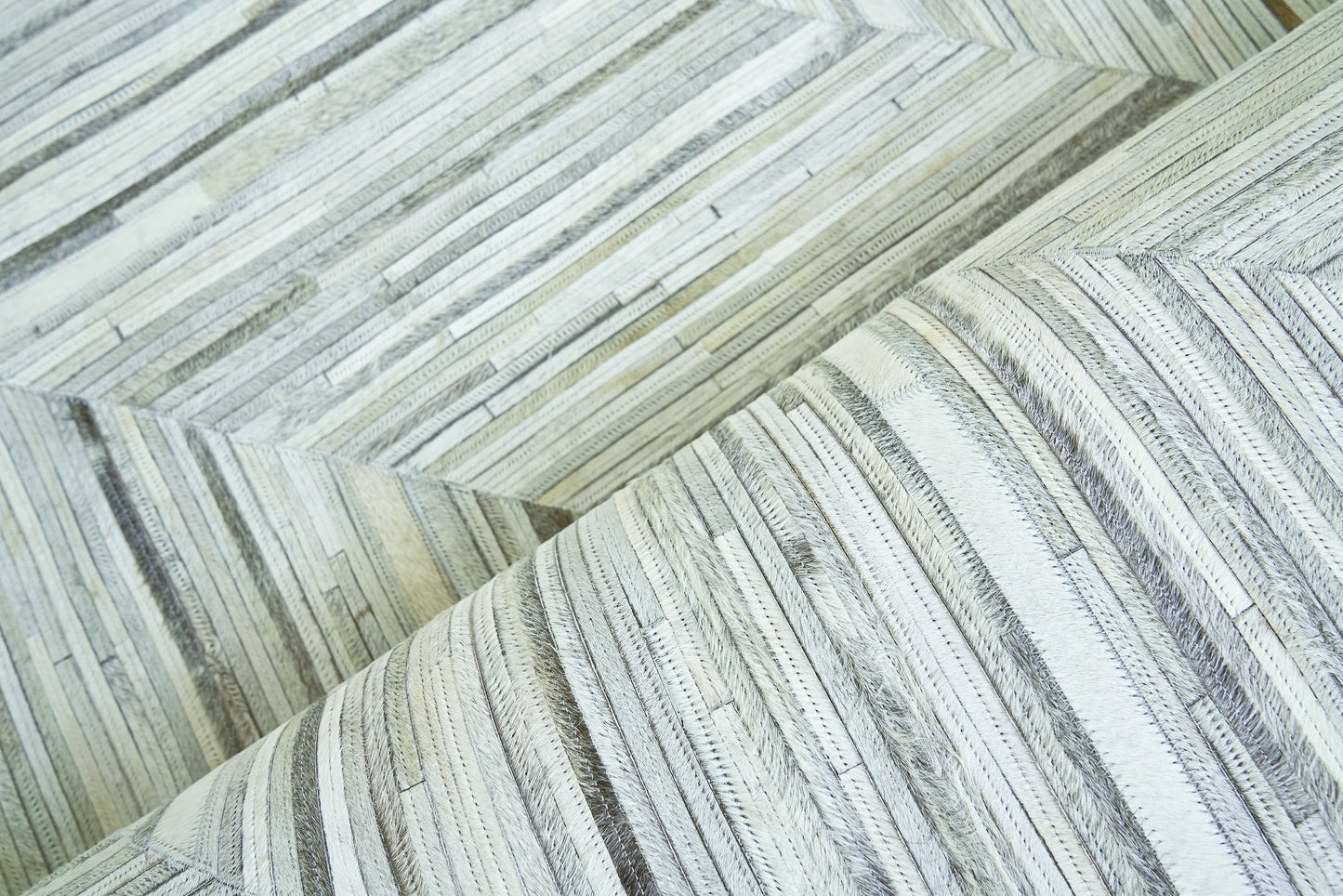Close-up of pale gray and cream natural-hide rug with a narrow, plank-like striped pattern and soft, textured surface; indoor hand-stitched rug, size 5' x 8'.