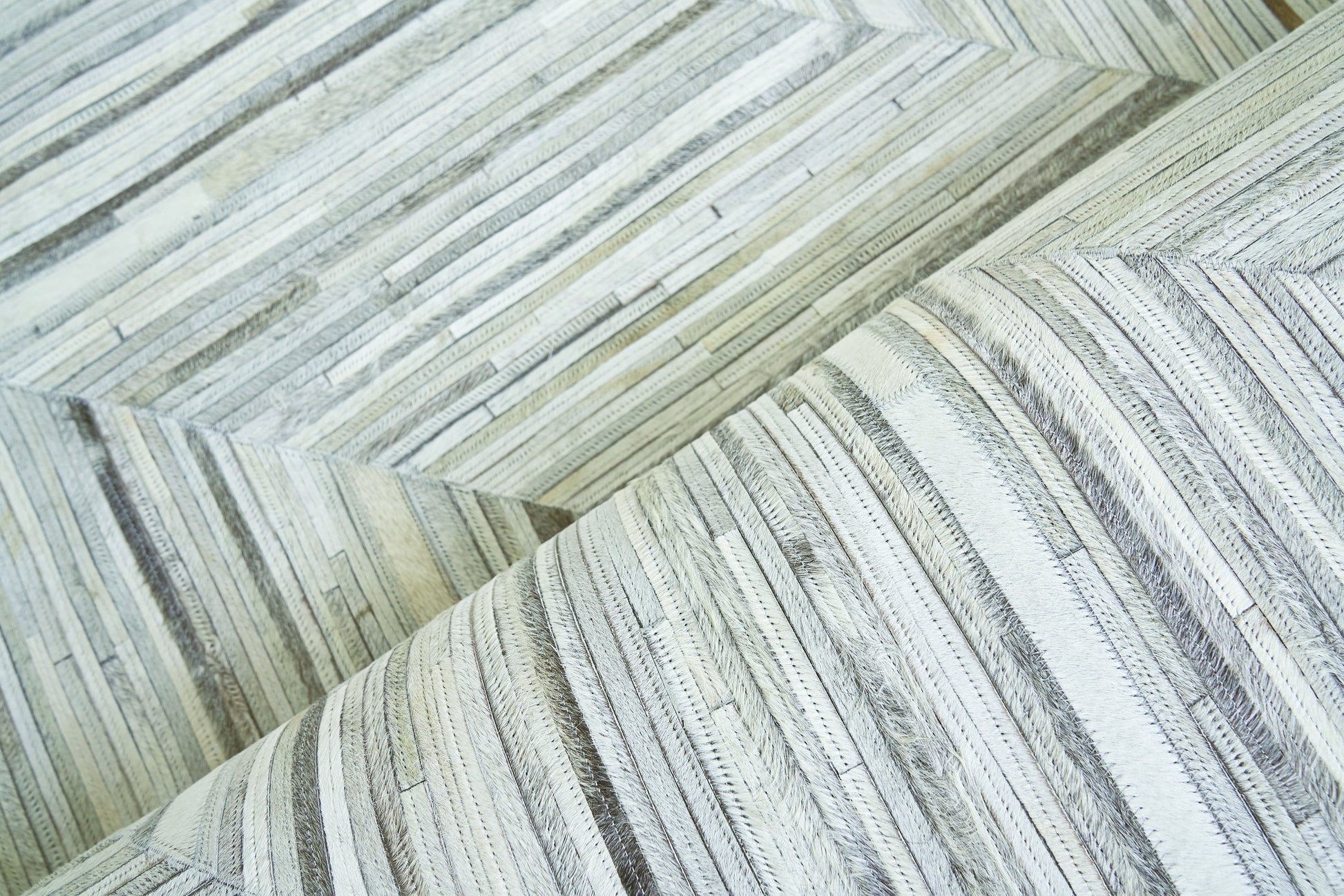 Close-up of pale gray and cream natural-hide rug with a narrow, plank-like striped pattern and soft, textured surface; indoor hand-stitched rug, size 5' x 8'.