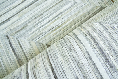 Close-up of pale gray and cream natural-hide rug with a narrow, plank-like striped pattern and soft, textured surface; indoor hand-stitched rug, size 5' x 8'.