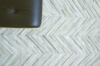 Partial view of a natural hide indoor hand-stitched rug on a light floor; size 5' x 8'.