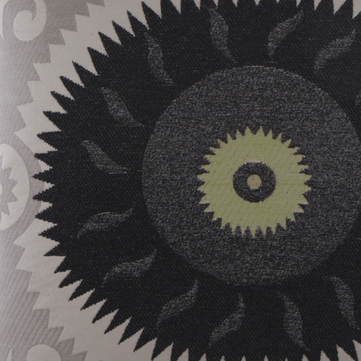 Close-up of fabric featuring a large black sunburst motif with olive-green center on a gray patterned background.