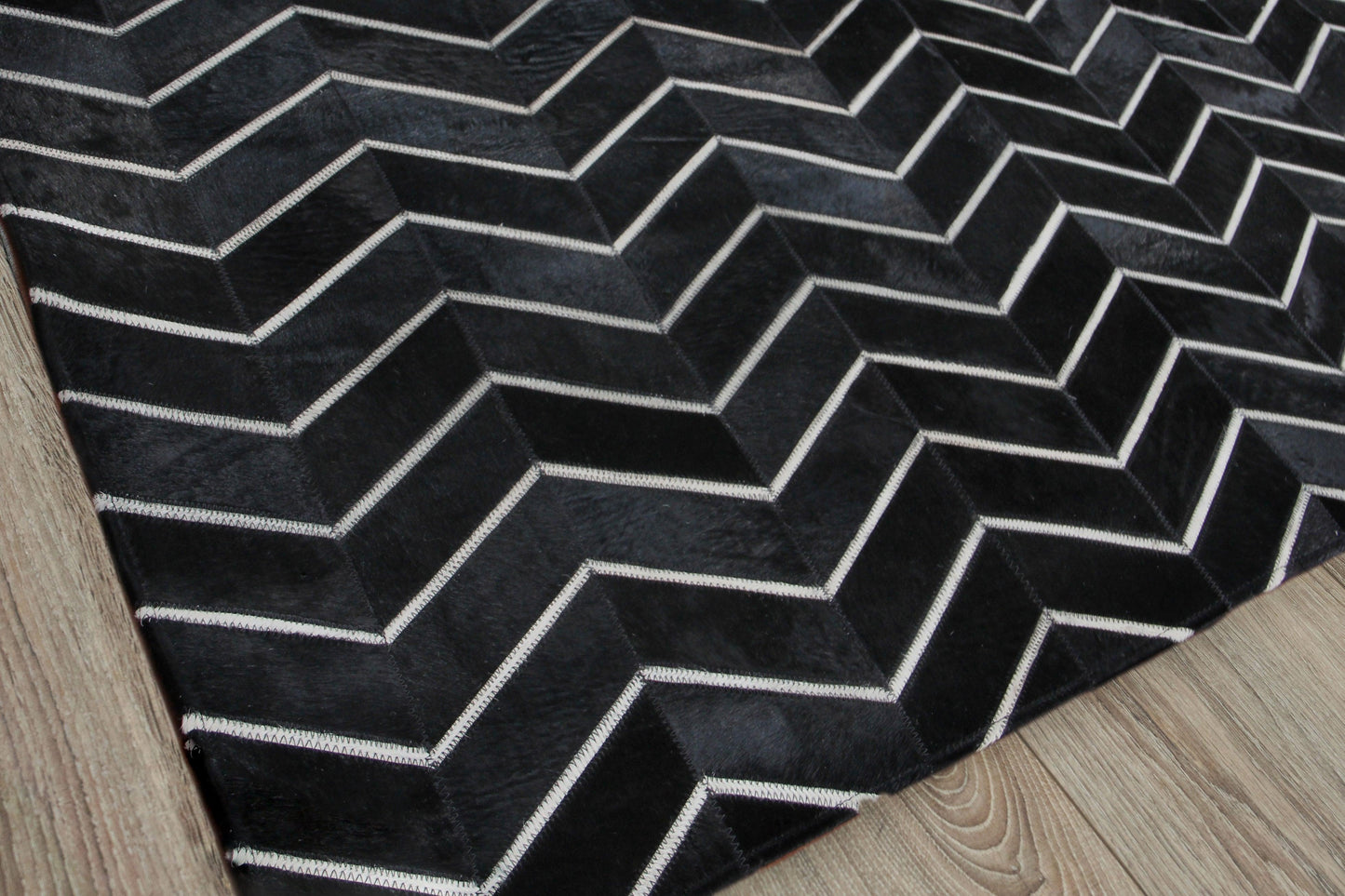 Natural hide indoor hand stitched rug; rectangular rug featuring a black background with white chevron zigzag pattern.