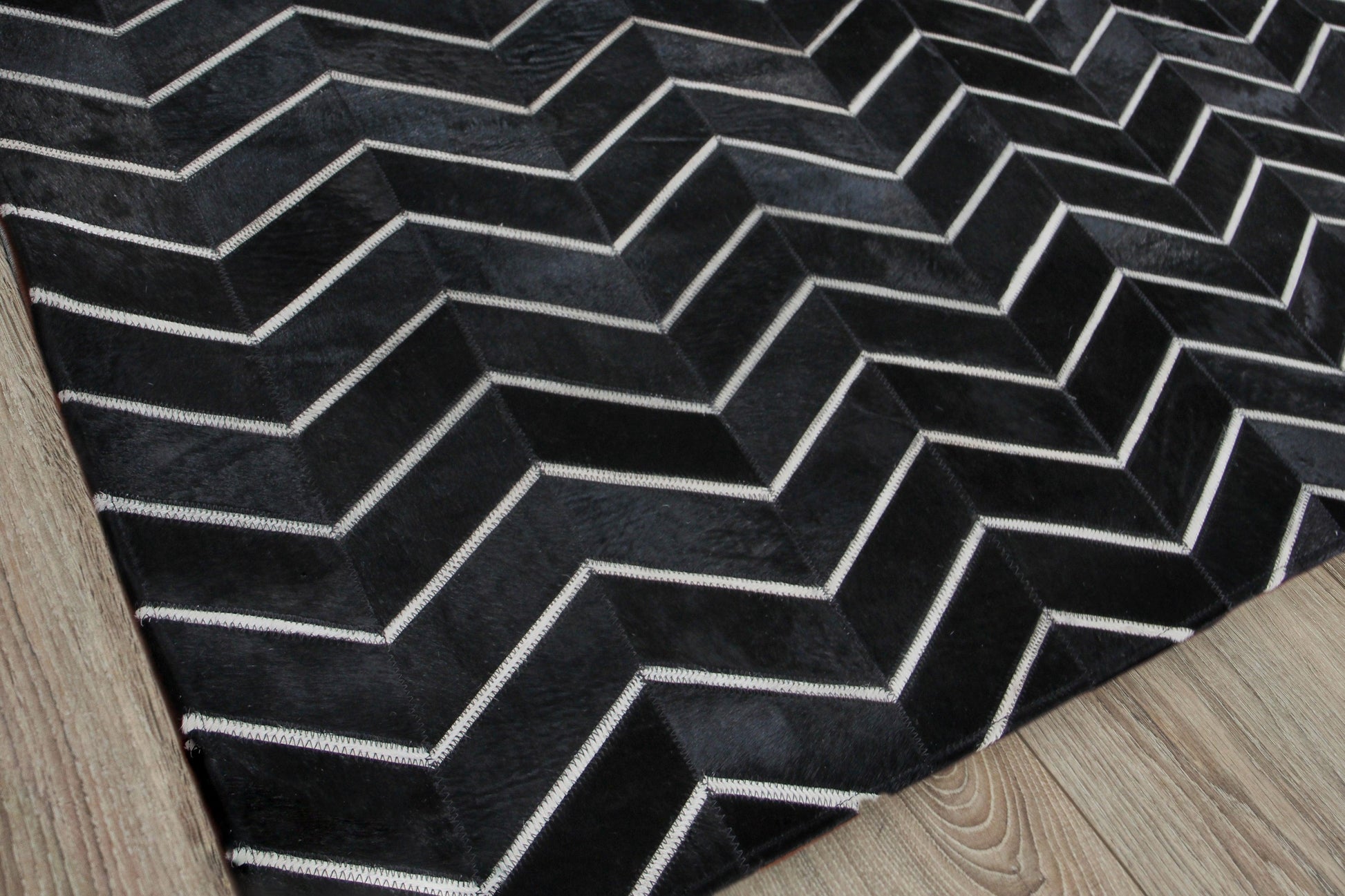 Natural hide indoor hand stitched rug; rectangular rug featuring a black background with white chevron zigzag pattern.