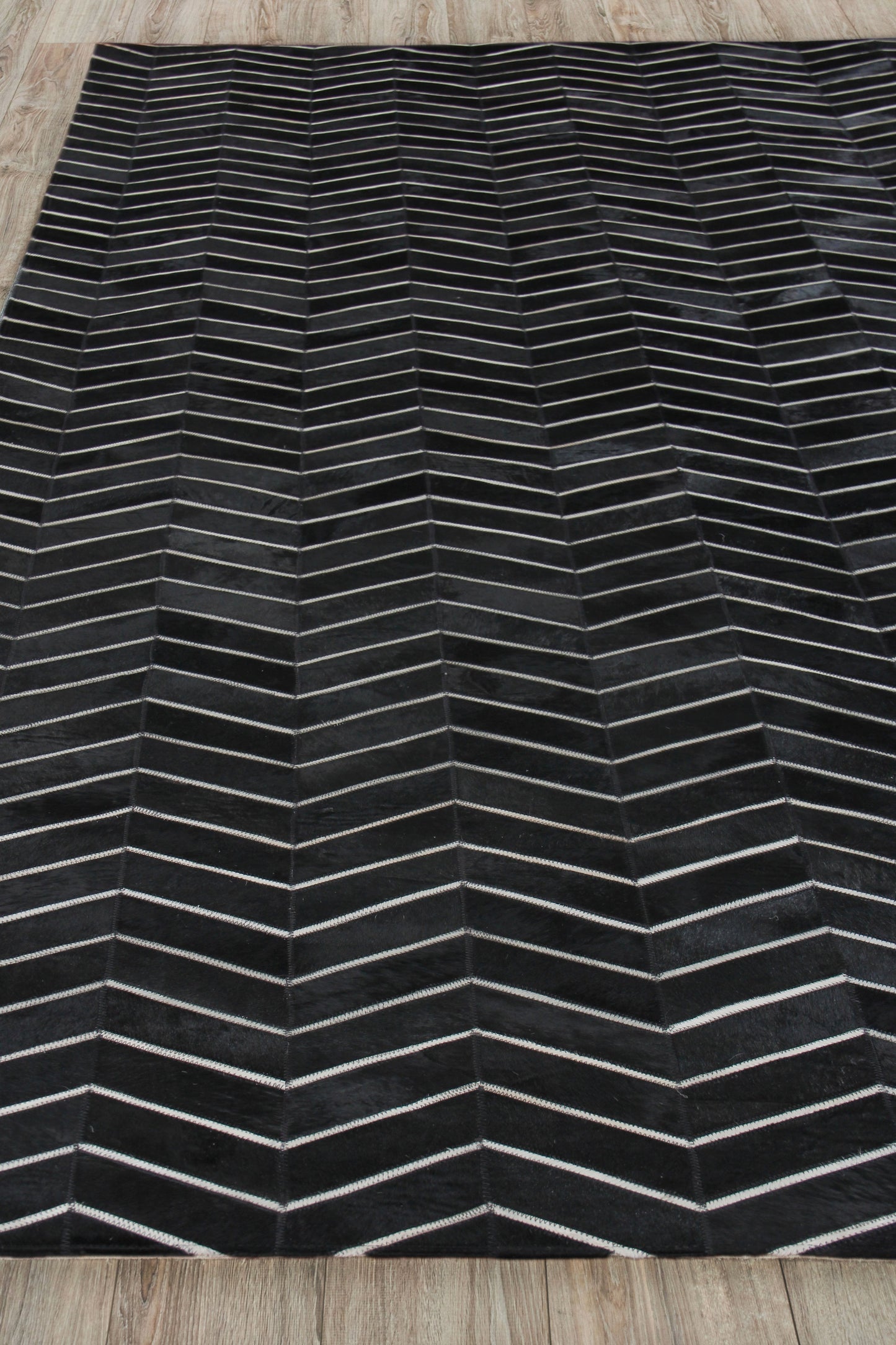 Rectangular black rug with light gray chevron lines forming a zigzag pattern on a wooden floor.