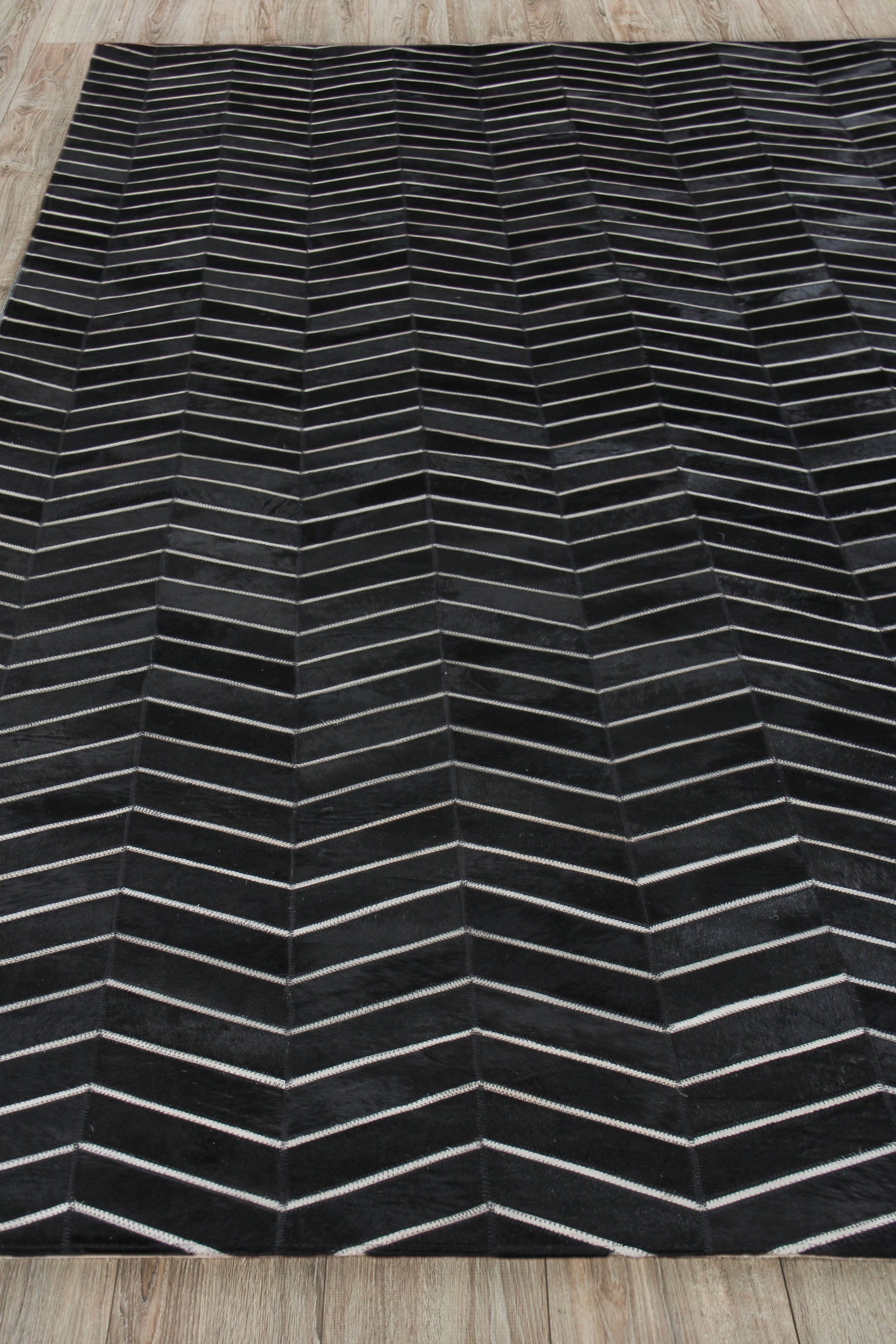 Rectangular black rug with light gray chevron lines forming a zigzag pattern on a wooden floor.