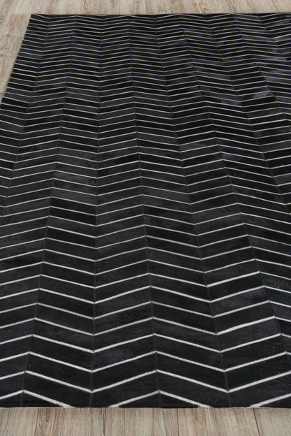 Rectangular black rug with light gray chevron lines forming a zigzag pattern on a wooden floor.