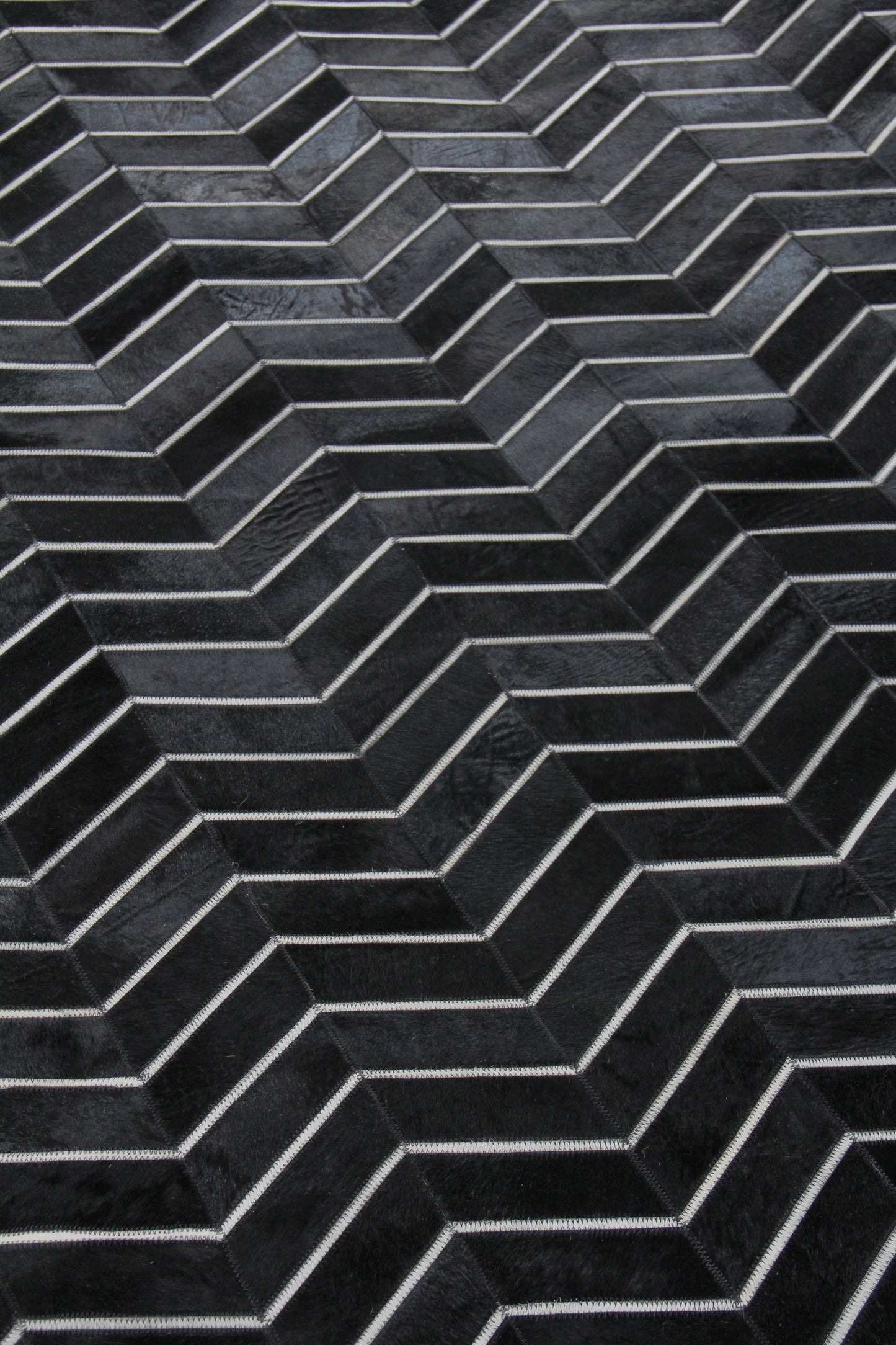 Close-up of a charcoal chevron rug with a dark herringbone pattern and visible hand-stitching.