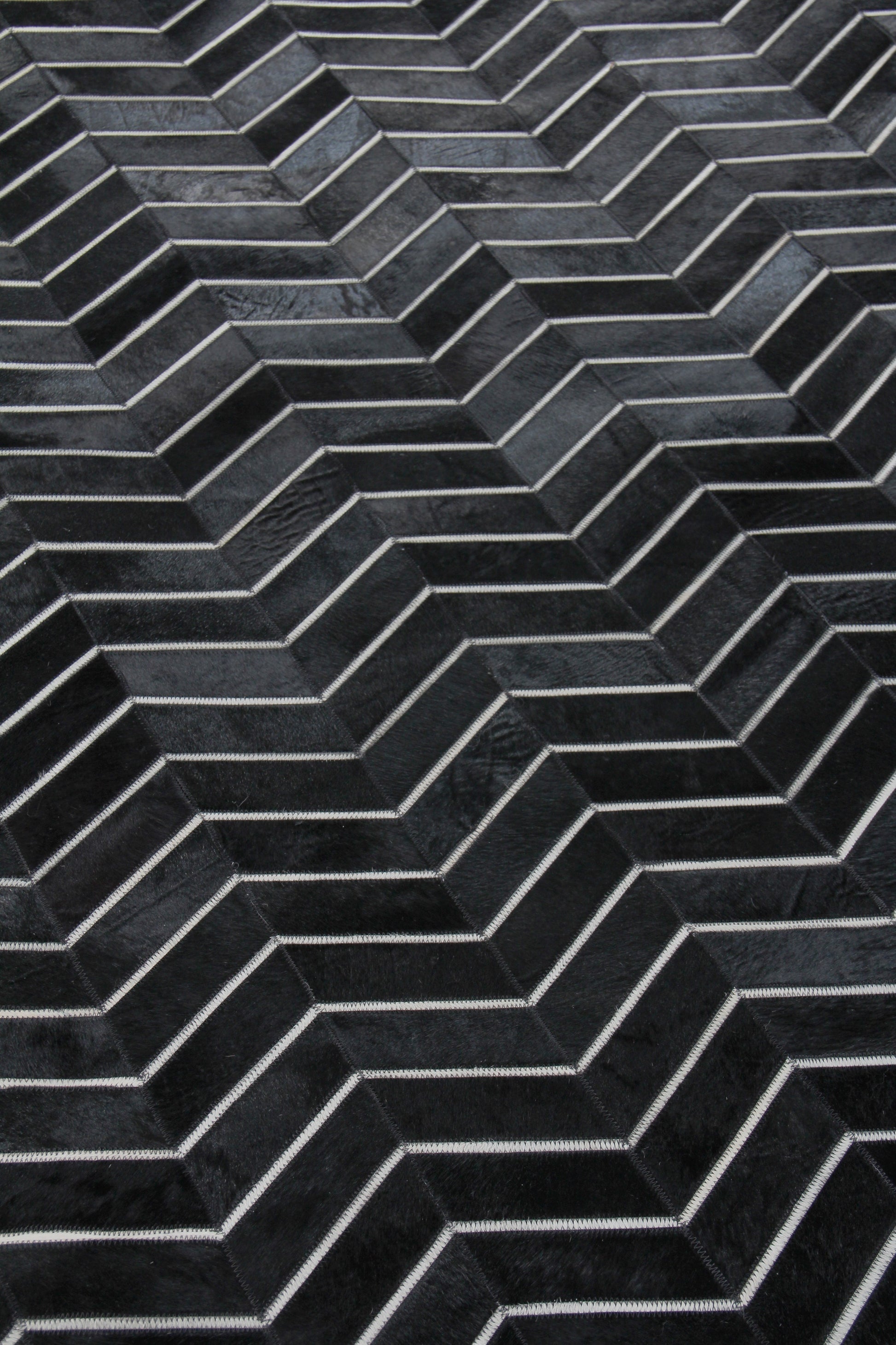 Close-up of a charcoal chevron rug with a dark herringbone pattern and visible hand-stitching.