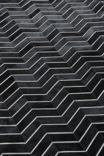 Close-up of a charcoal chevron rug with a dark herringbone pattern and visible hand-stitching.