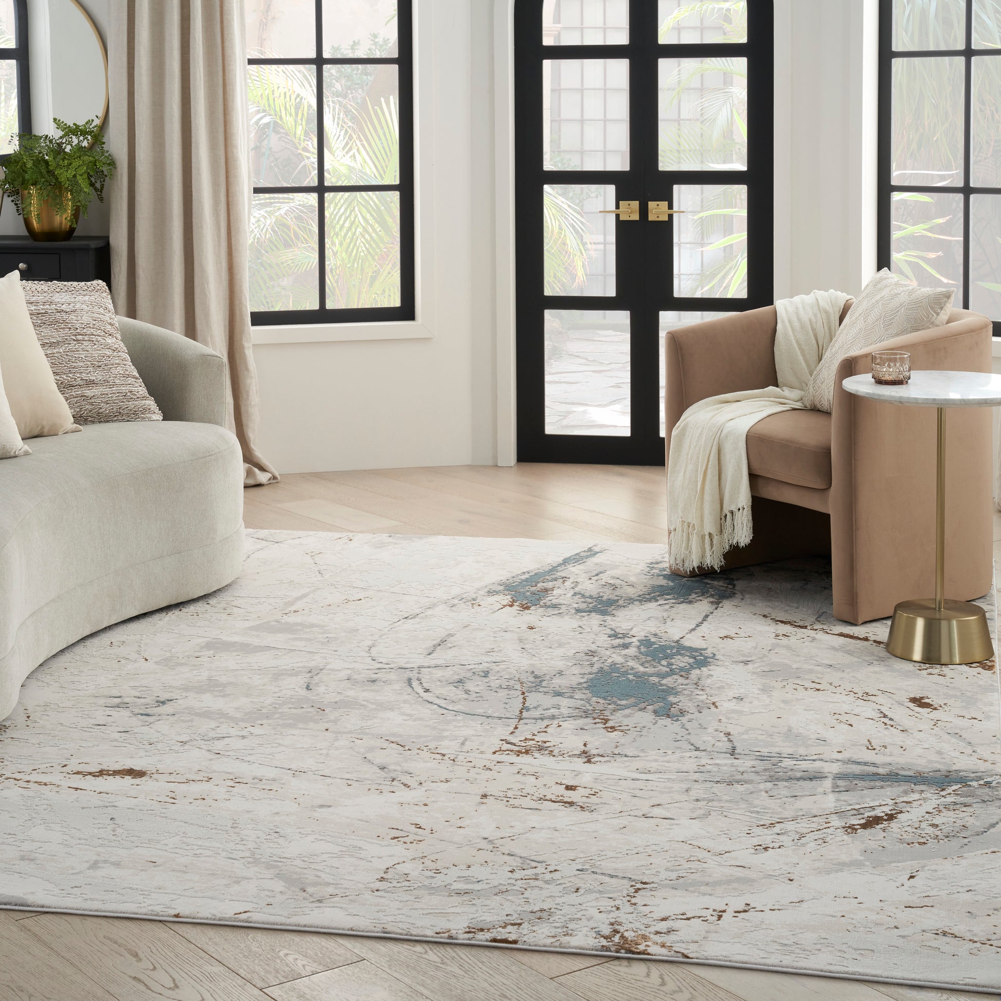 Bright living room with abstract rug, beige sofa, blush armchair, marble side table with brass base, and black doors.