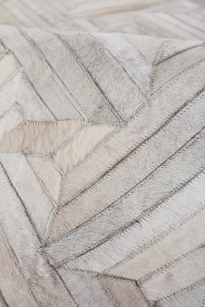 Natural hide rug with chevron patchwork in grey and beige tones; indoor, hand-stitched details.