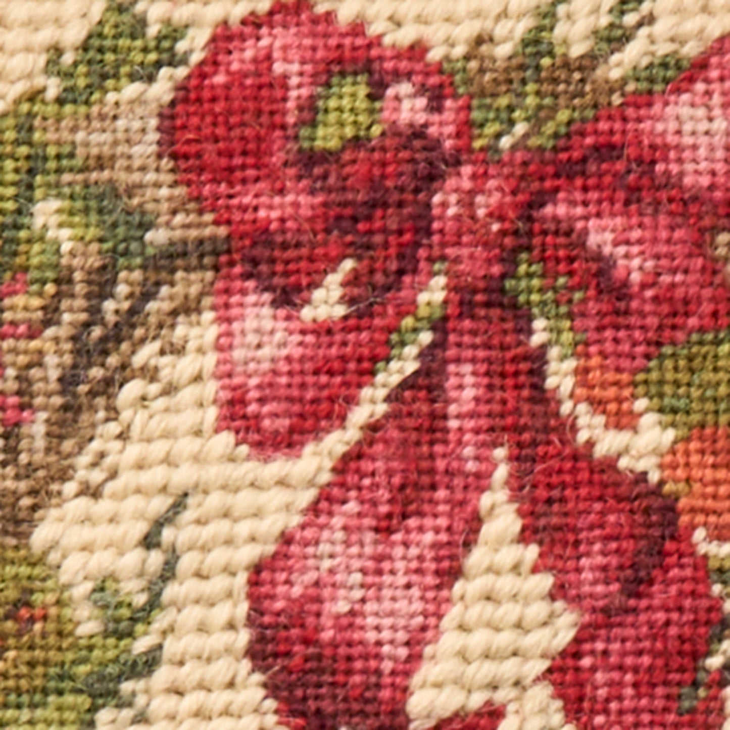 Close-up woven tapestry fabric featuring red flowers on a cream background with green leaves.