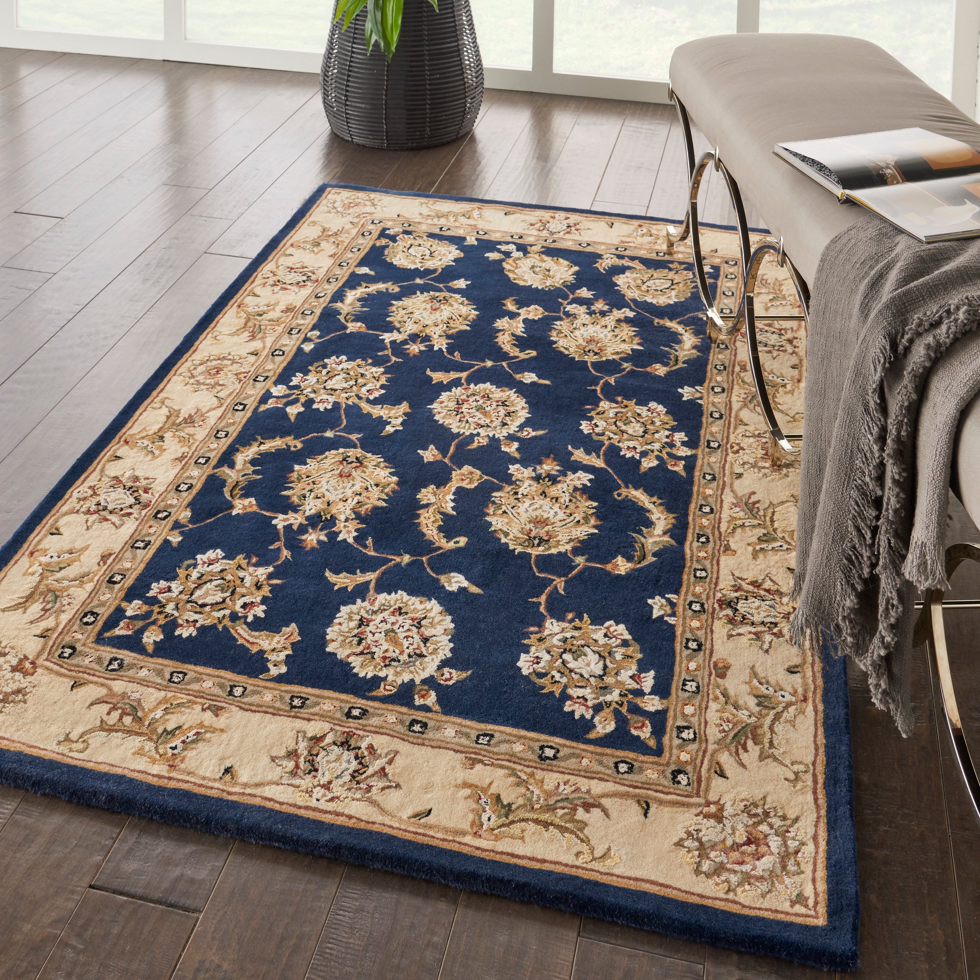 Rectangular traditional oriental area rug with navy field and cream floral motifs, beige border on dark hardwood floor.