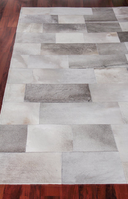 Rectangular patchwork area rug with stone-like gray and white blocks on dark wood floor.
