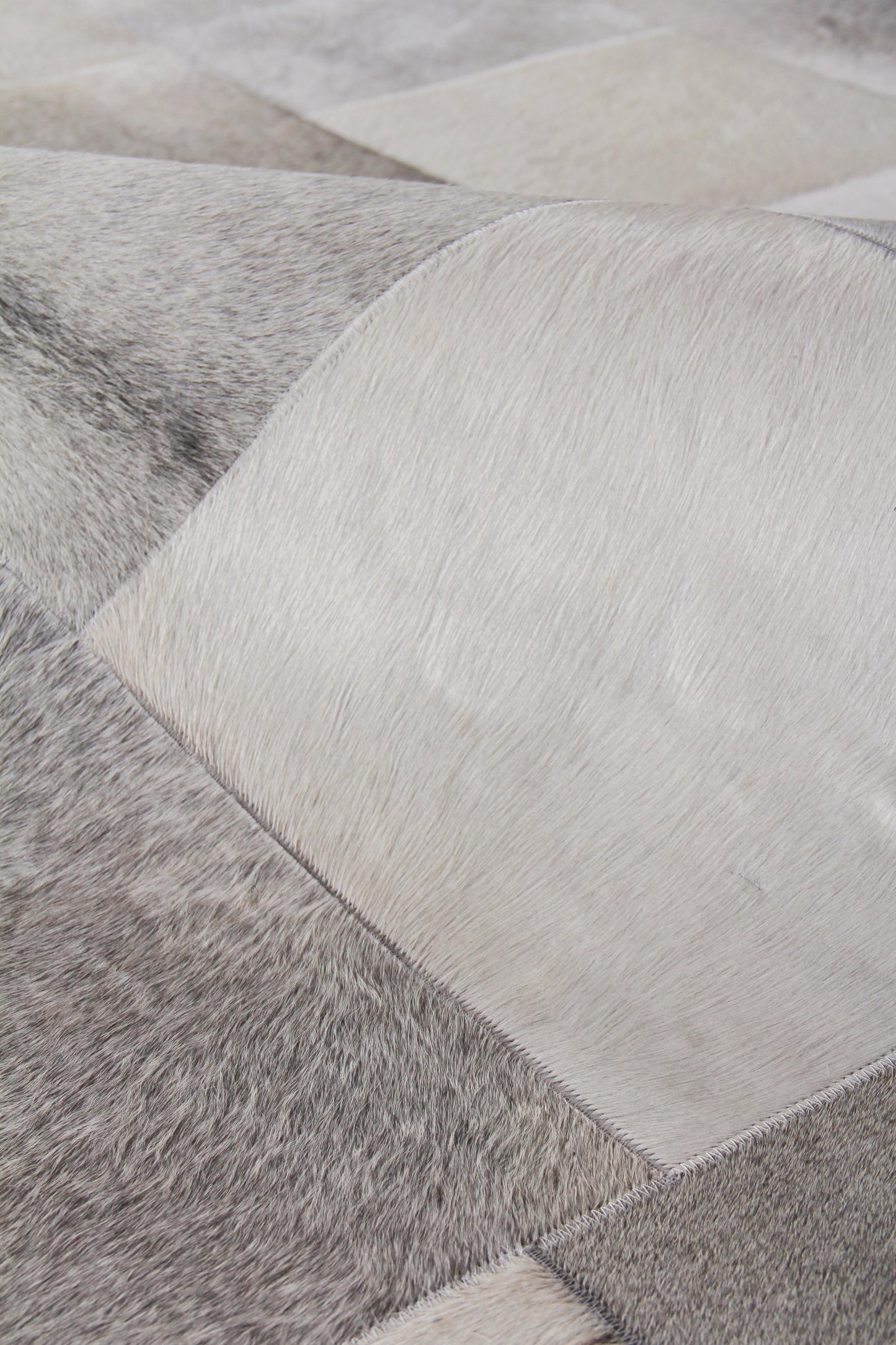 Close-up of a patchwork natural hide rug with grey and white square panels, hand-stitched.