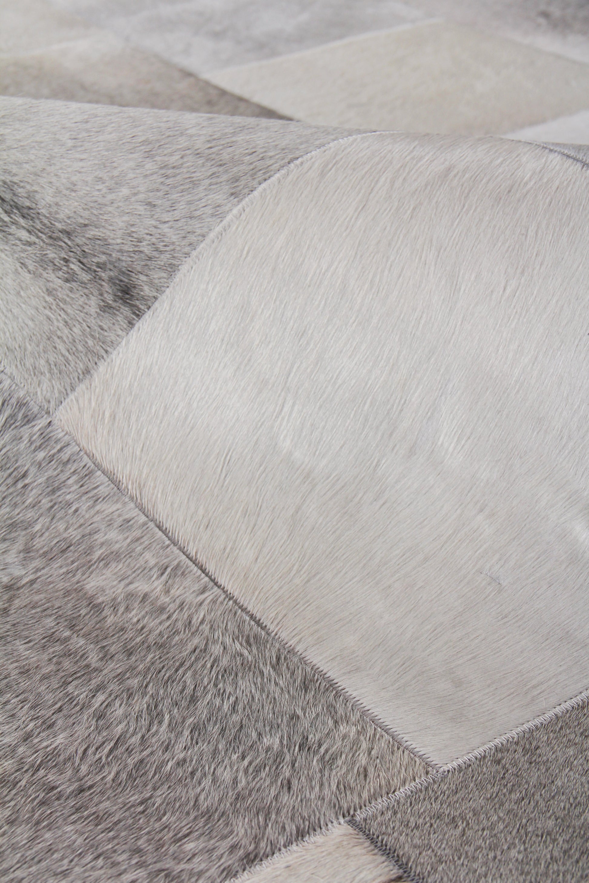 Close-up of a patchwork natural hide rug with grey and white square panels, hand-stitched.