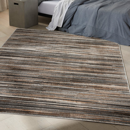 Rectangular striped area rug in brown, tan & gray tones under a bed with gray bedding, modern bedroom decor.
