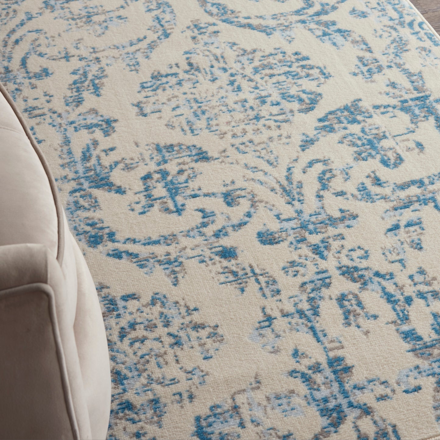 Beige area rug with a distressed blue floral/arabesque pattern; partial beige chair on the left.