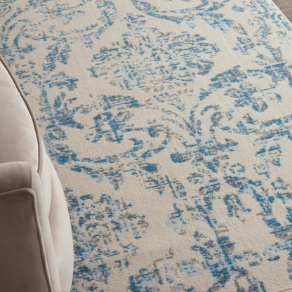 Beige area rug with a distressed blue floral/arabesque pattern; partial beige chair on the left.