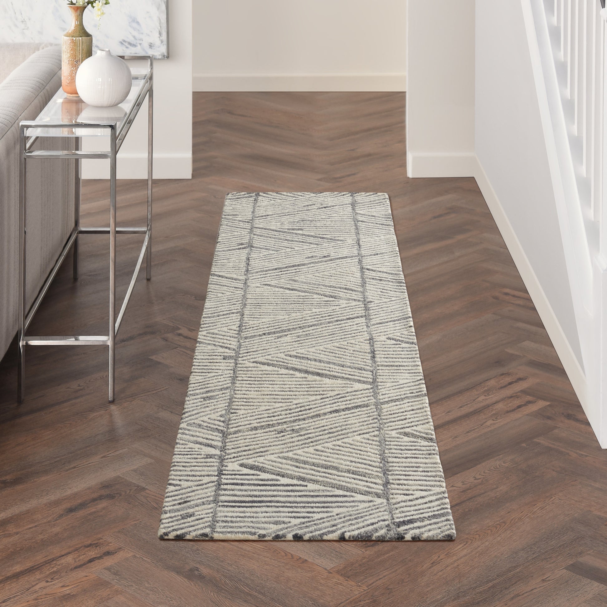 Light gray geometric hallway runner rug with darker diagonal lines on a dark wood herringbone floor.