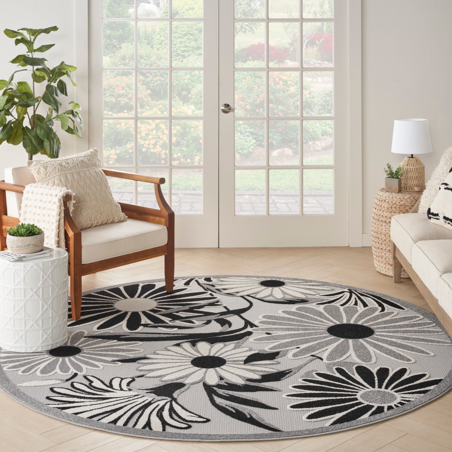Round area rug with large black and white floral pattern on gray, placed in a bright living room beside chair and sofa.