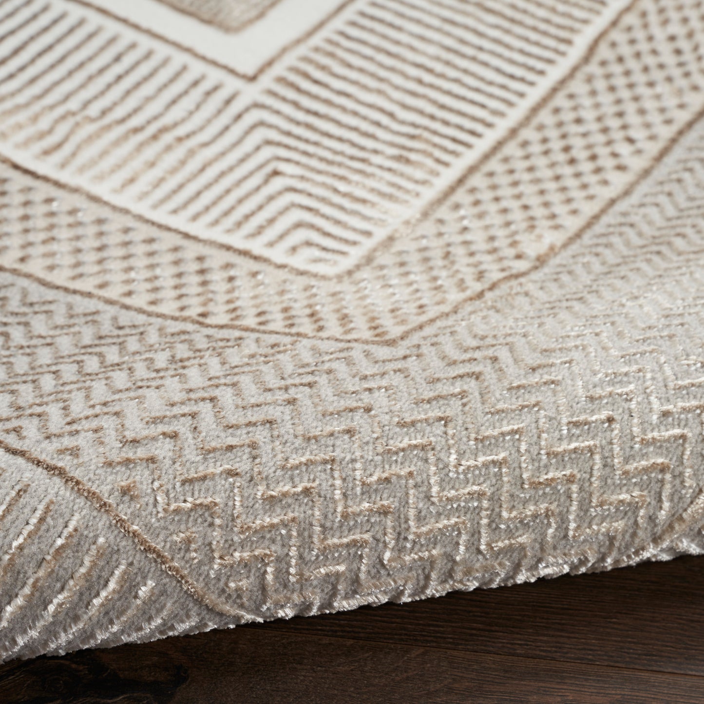 Beige textured area rug with raised geometric chevrons and rectangular patterns on wood floor.