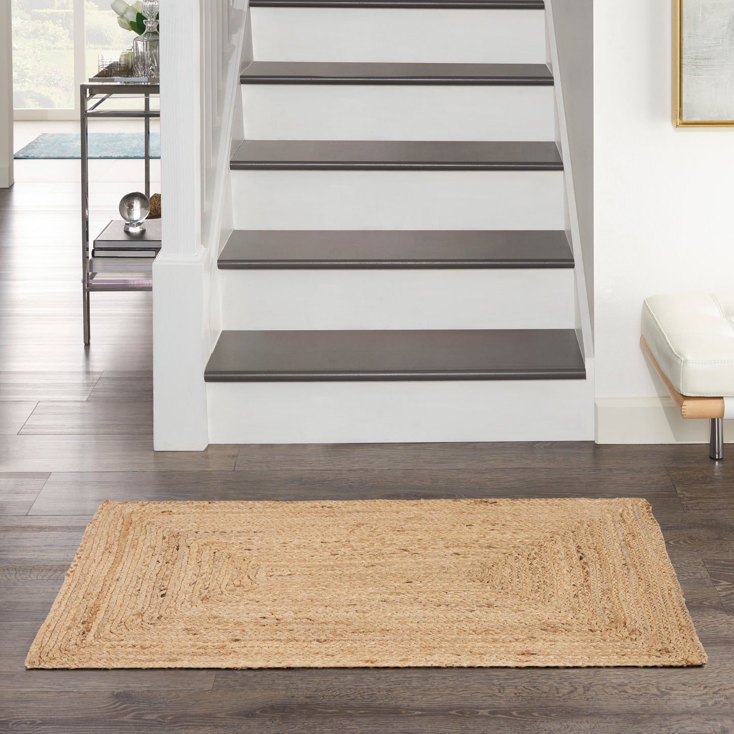 Entryway with white staircase featuring dark wooden treads and a natural jute rug on dark hardwood floor.