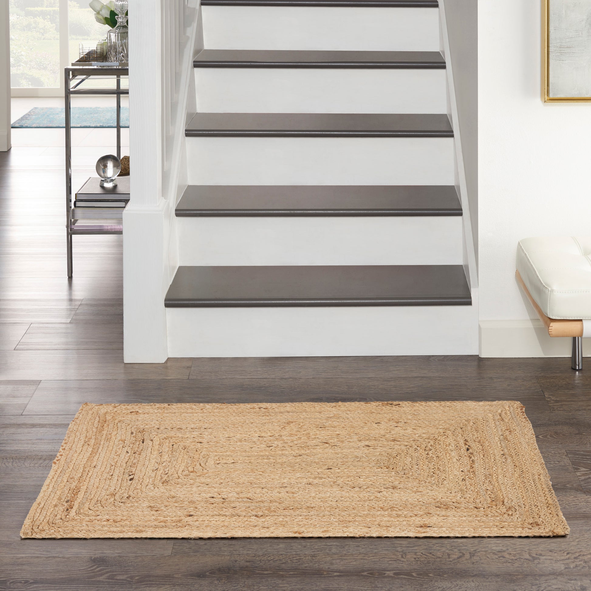 Entryway with white staircase featuring dark wooden treads and a natural jute rug on dark hardwood floor.