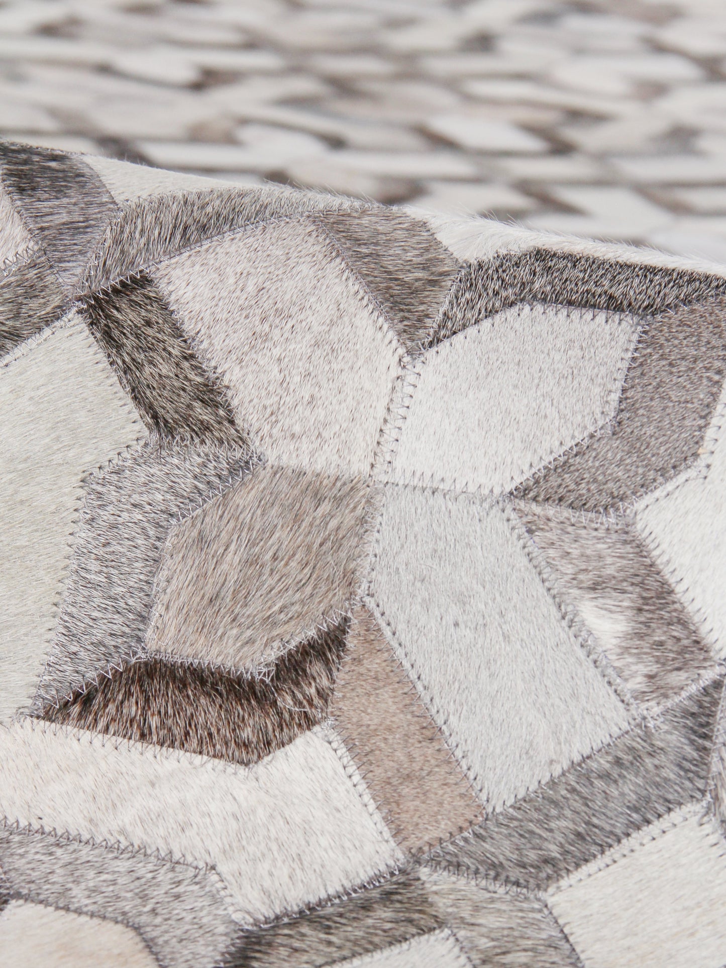 Geometric patchwork natural hide rug in neutral grays, creams and beiges with hexagonal panels.
