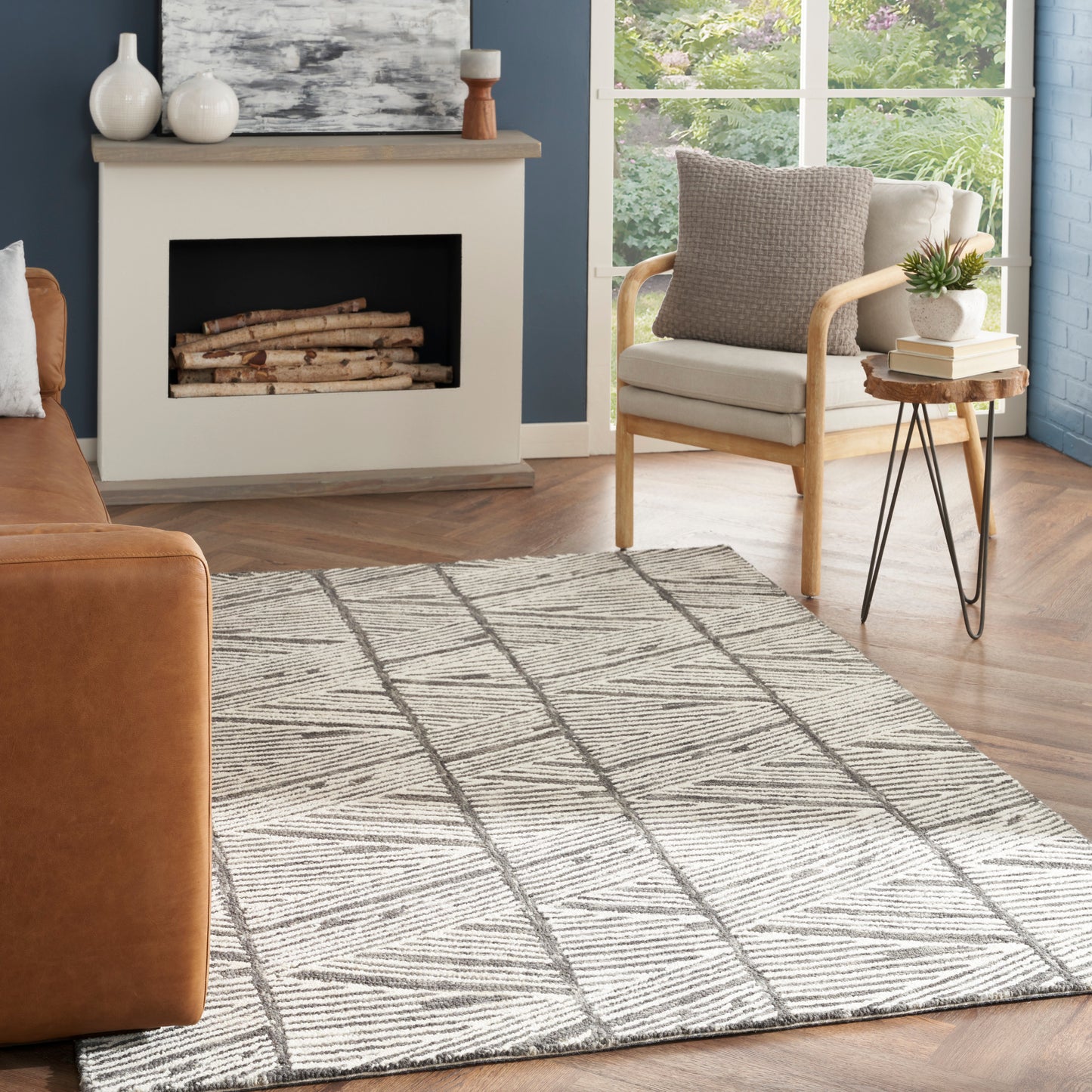 Geometric beige-gray area rug with dark lines in a cozy living room featuring a tan sofa, light-wood chair, and fireplace.